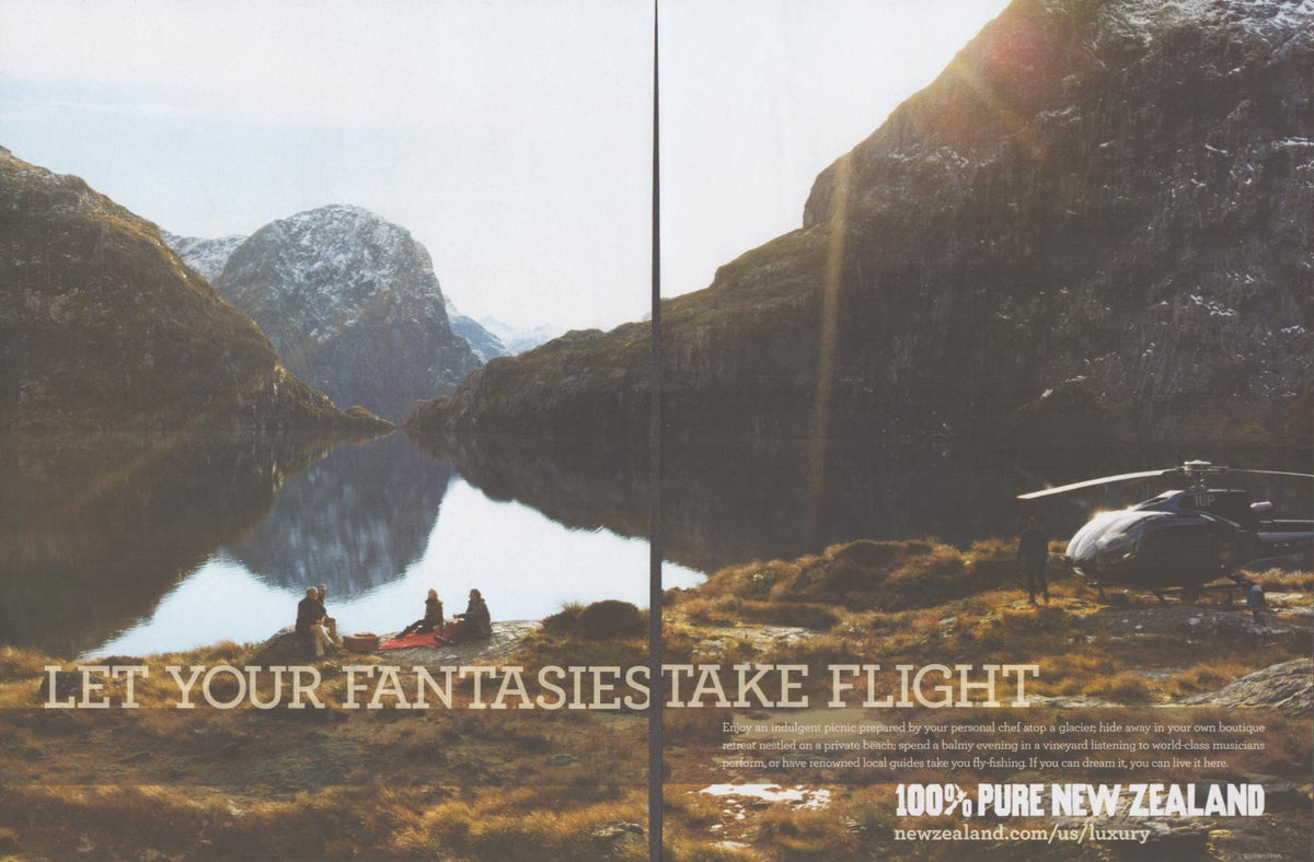 Vintage 2000s Tourism New Zealand original print advertisement, two-page spread showing couple picnicking beside glacial alpine lake with private helicopter and dramatic mountain peaks