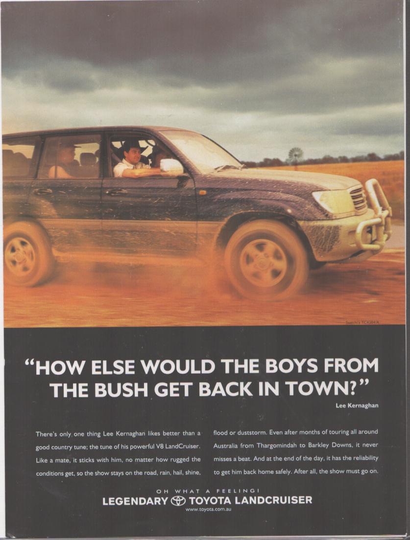 Vintage 1990s Toyota LandCruiser original print advertisement, Lee Kernaghan driving muddy V8 SUV across red Australian outback dirt road under stormy sky