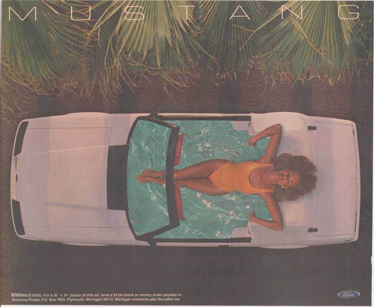 Vintage 1983 Ford Mustang convertible original print advertisement, aerial overhead view of woman in orange swimsuit lounging inside white open-top Mustang with palm trees above