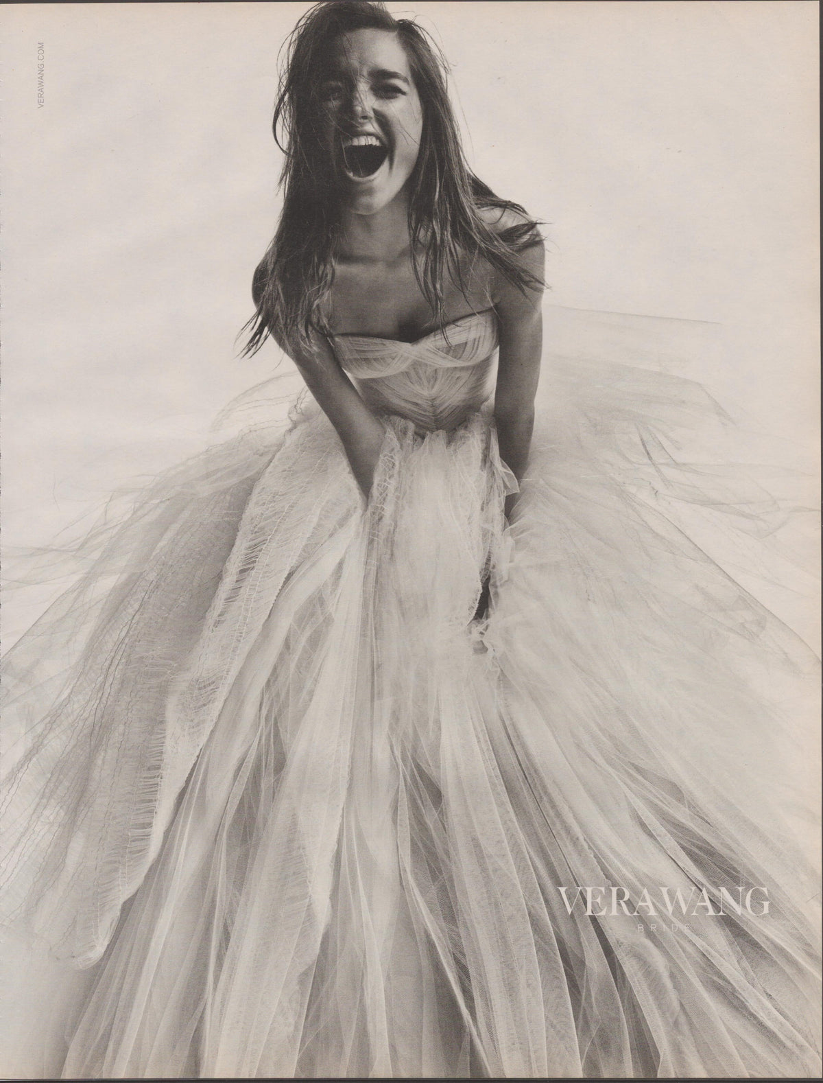 Vintage 2000s Vera Wang Bridal original print advertisement, black and white image of laughing model in billowing tulle ball gown with windswept hair