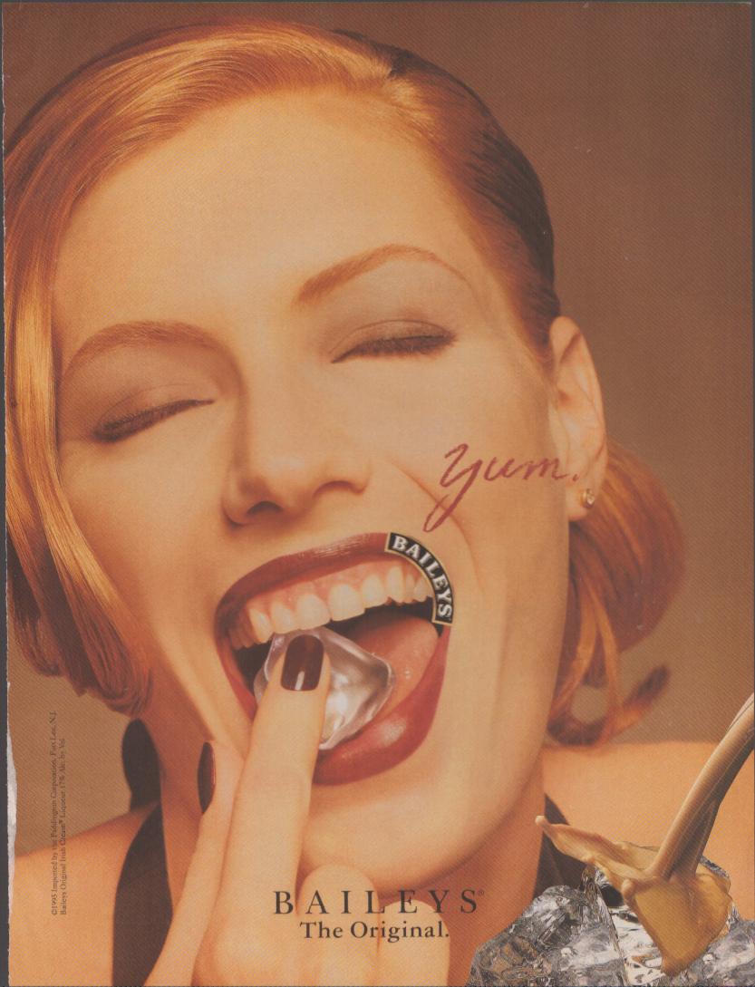 Vintage 1990s Baileys Irish Cream original print advertisement, close-up of red-haired woman savoring a Baileys-branded ice cube with the word 'yum' and liqueur pouring over ice