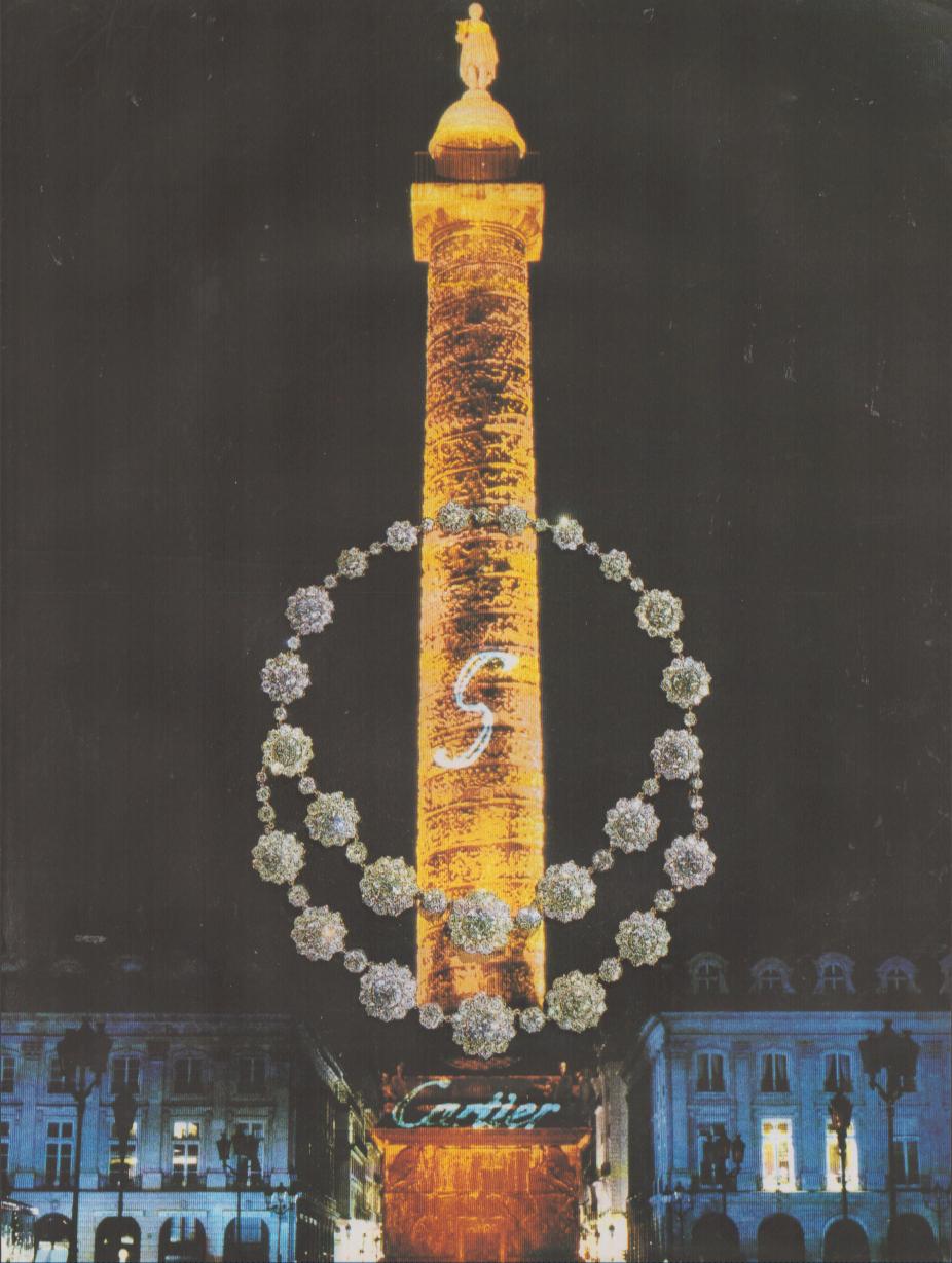 Vintage 1970s Cartier Place Vendôme original print advertisement, illuminated Colonne Vendôme at night with oversized diamond necklace composited around the column and Cartier boutique sign glowing below