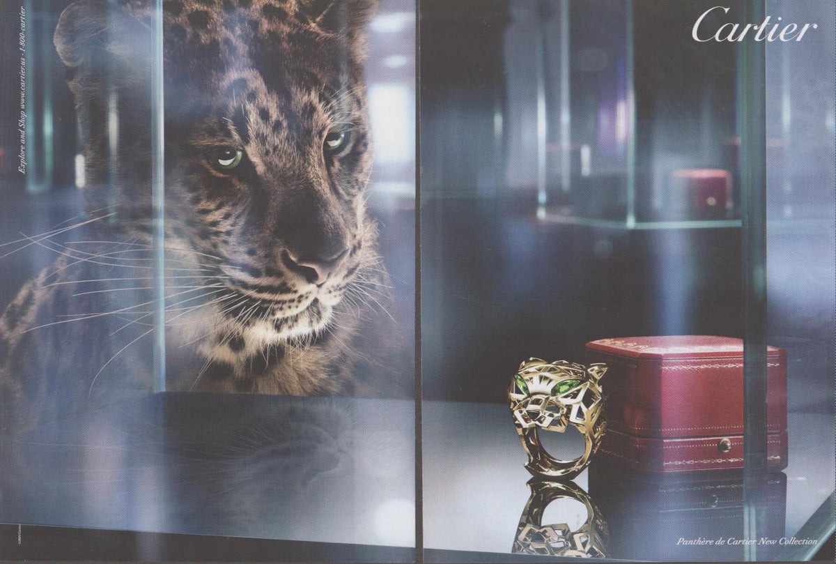 Vintage 2000s Cartier Panthère de Cartier original print advertisement, close-up leopard face peering through glass vitrine at gold panther ring beside red Cartier box