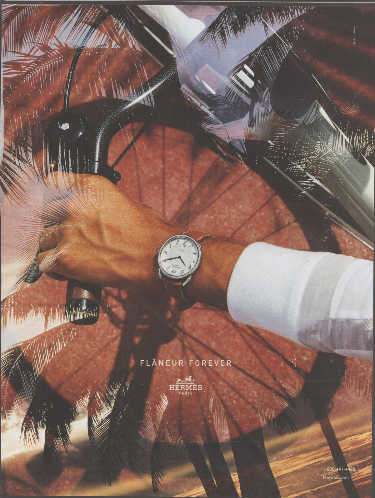 Vintage 2000s Hermès Flâneur Forever original print advertisement, man's wrist wearing Hermès watch gripping bicycle handlebar with tropical palm tree double-exposure background