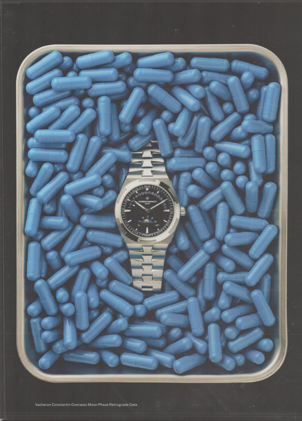 Vintage 2000s Vacheron Constantin Overseas Moon Phase Retrograde Date original print advertisement, steel sport watch resting among blue capsules on a clinical tray against dark background