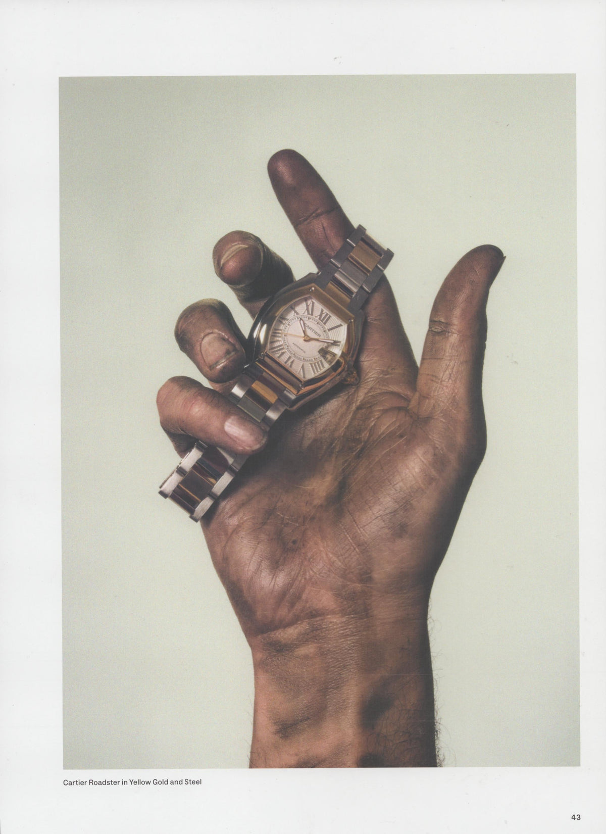 Vintage 2002 Cartier Roadster original print advertisement, close-up of weathered hand holding yellow gold and steel watch against pale background