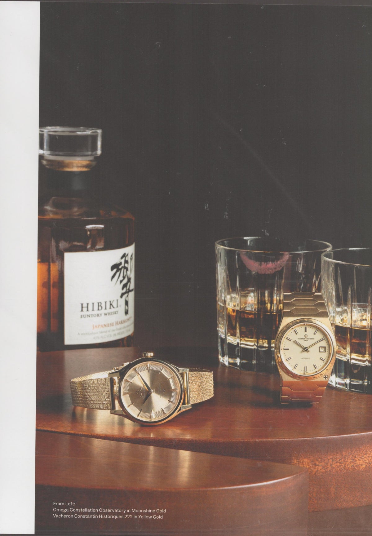 Vintage 1990s Omega Constellation and Vacheron Constantin 222 original print advertisement, two gold watches on mahogany table beside Hibiki Suntory whisky bottle and crystal glasses against dark background