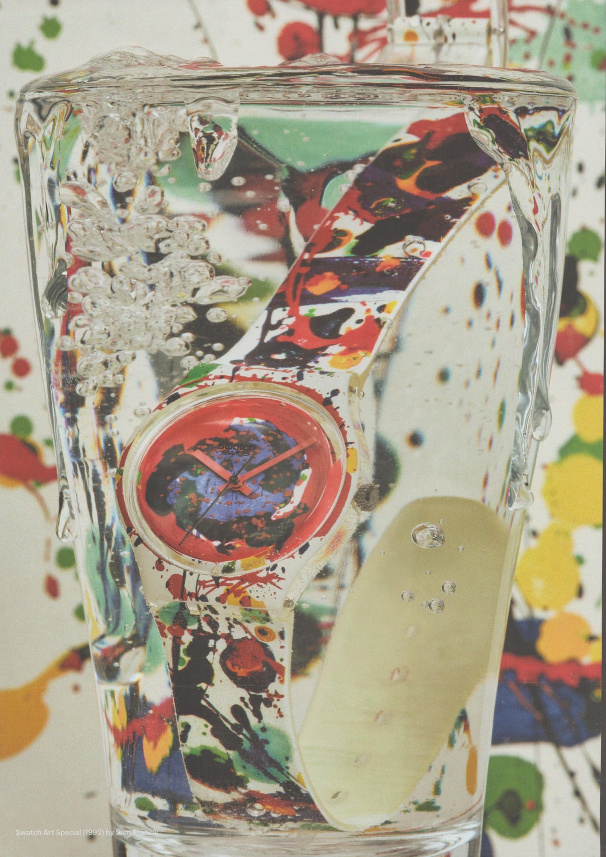 Vintage 1992 Swatch Art Special Sam Francis original print advertisement, colorful paint-splattered watch submerged in a clear glass of water against an abstract splatter background