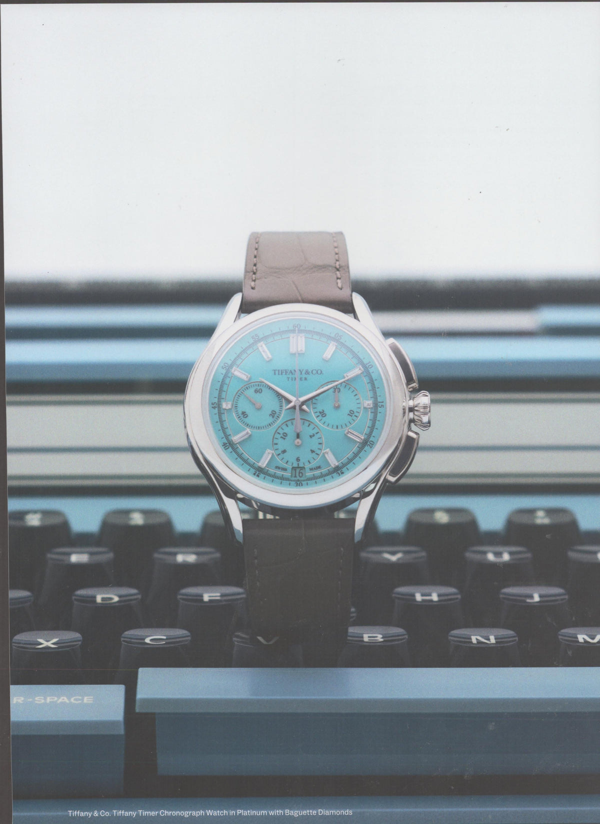 Vintage 1990s Tiffany & Co. Timer Chronograph original print advertisement, iconic Tiffany Blue dial watch on platinum case resting on vintage typewriter keys