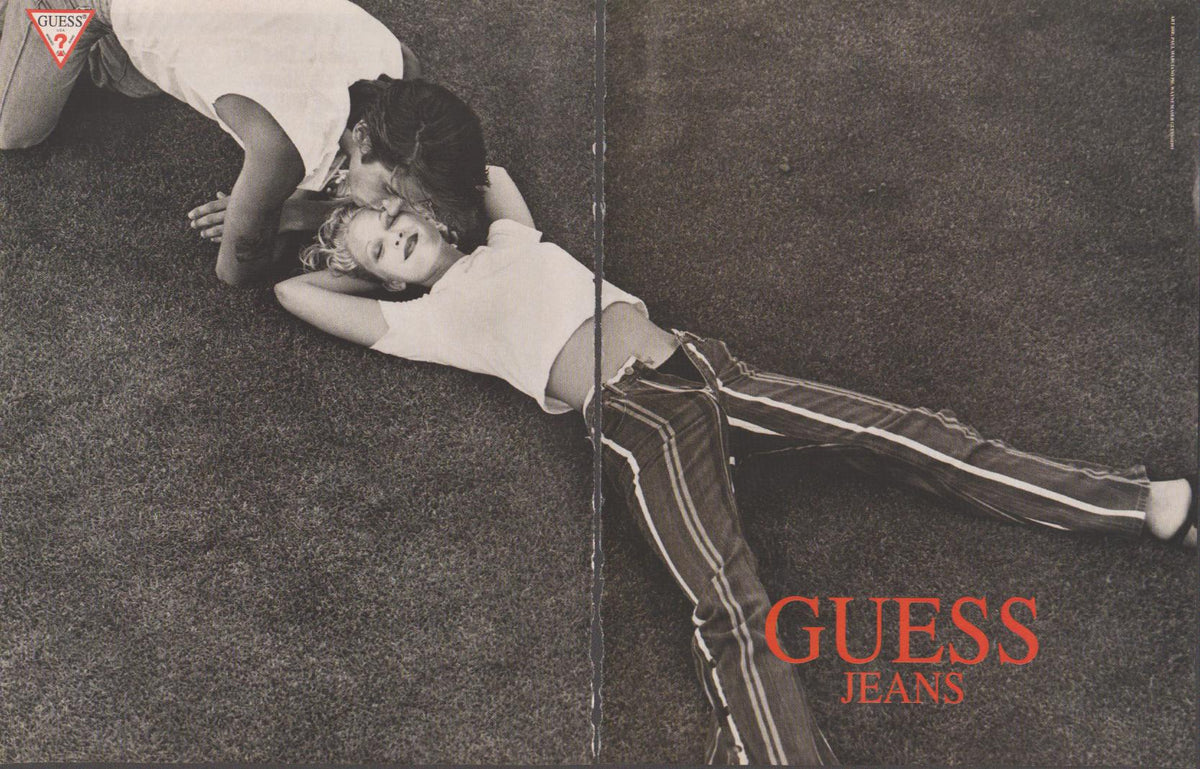 Vintage 1980s Guess Jeans original print advertisement, black and white two-page spread with couple posed on grass, bold red Guess Jeans logo