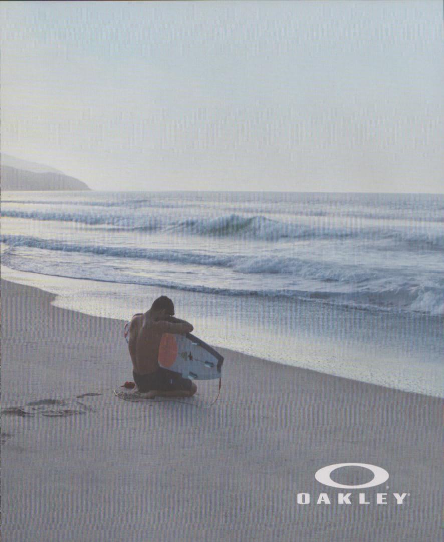 Vintage 1990s Oakley original print advertisement, lone surfer kneeling on misty beach with surfboard watching ocean waves