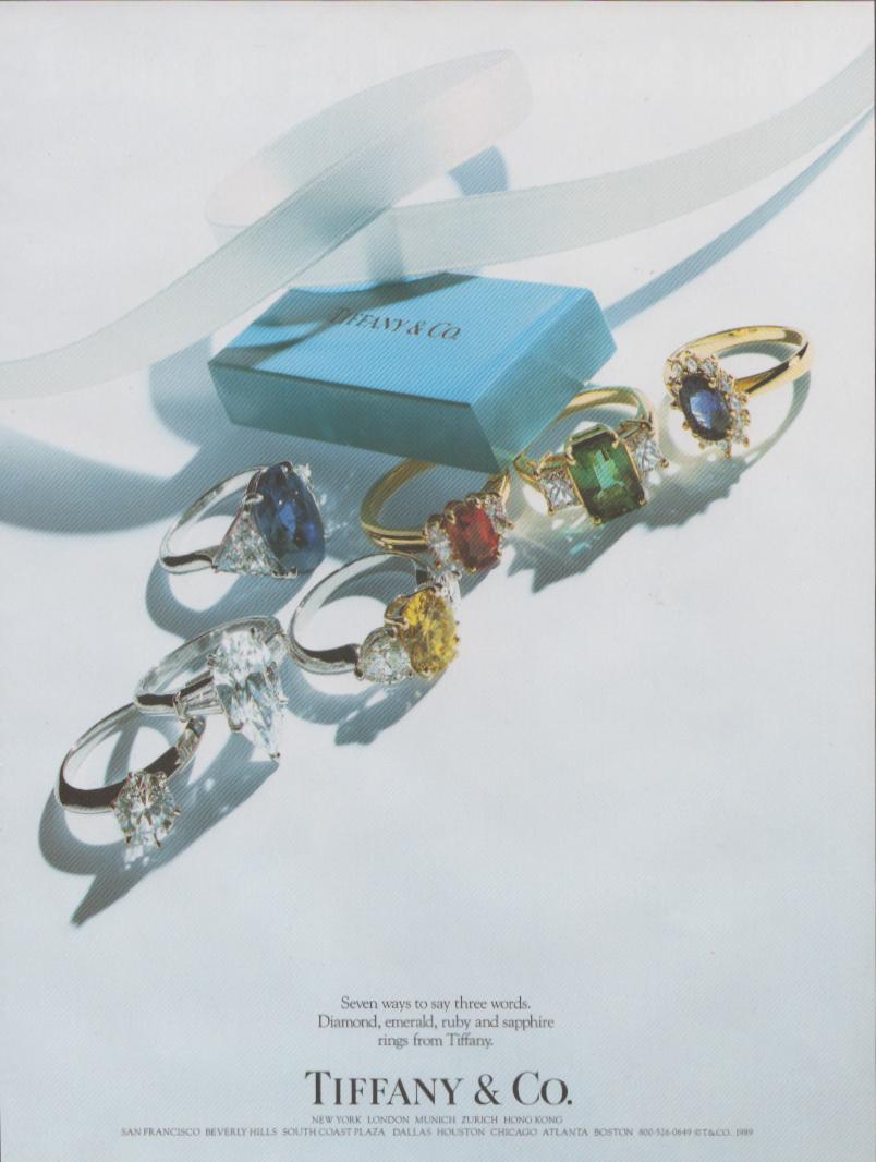 Vintage 1989 Tiffany &amp; Co. original print advertisement, seven gemstone rings including diamond, emerald, ruby and sapphire surrounding iconic Tiffany blue gift box with white ribbon on pale blue background